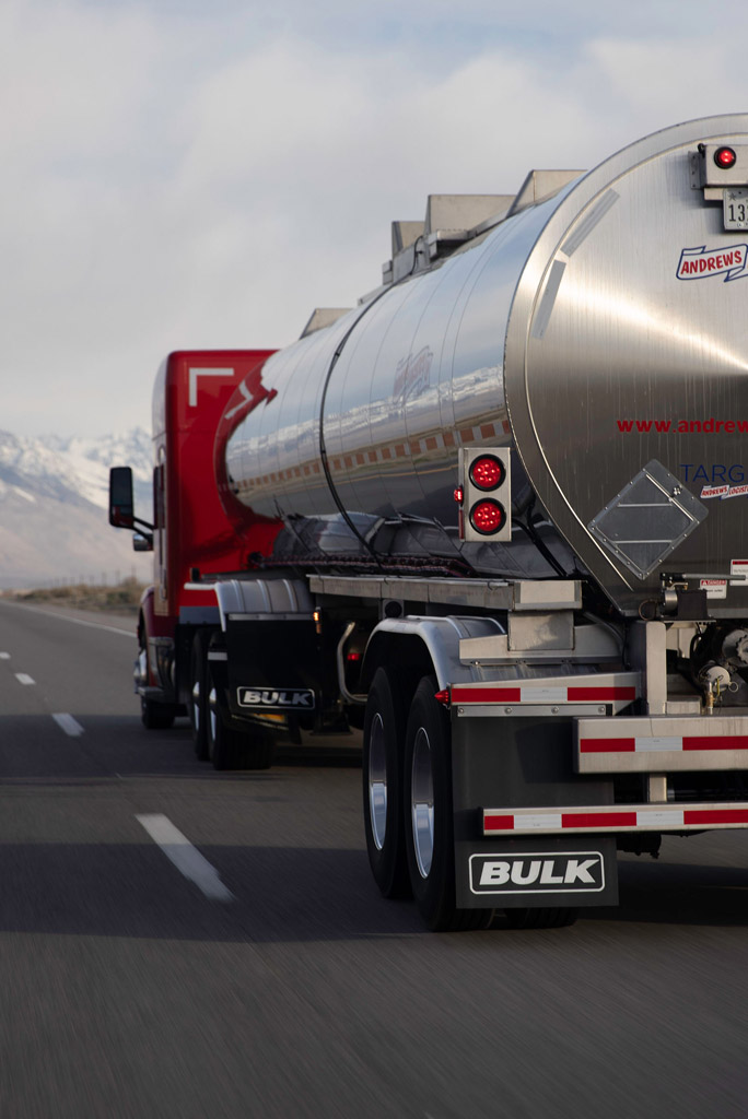 Rear view of an Andrews Logistics stainless steel tank trailer traveling a mountain highway