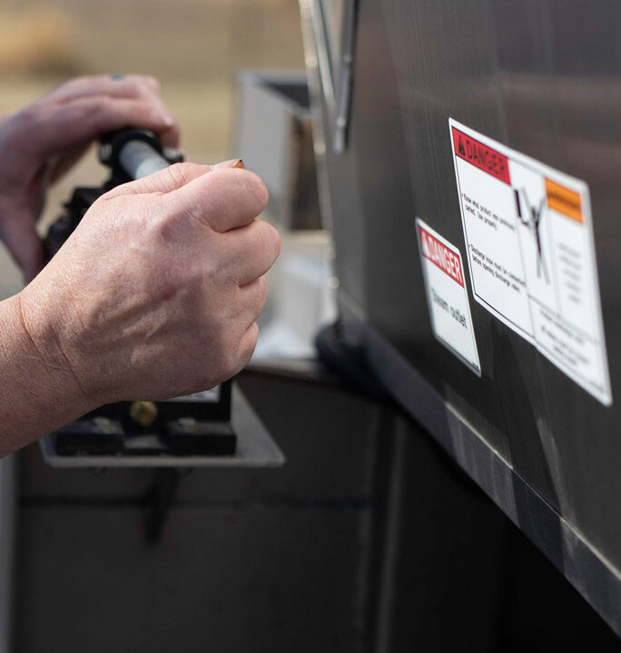 Driver operating a valve on a tank trailer beside hazardous materials danger warning labels