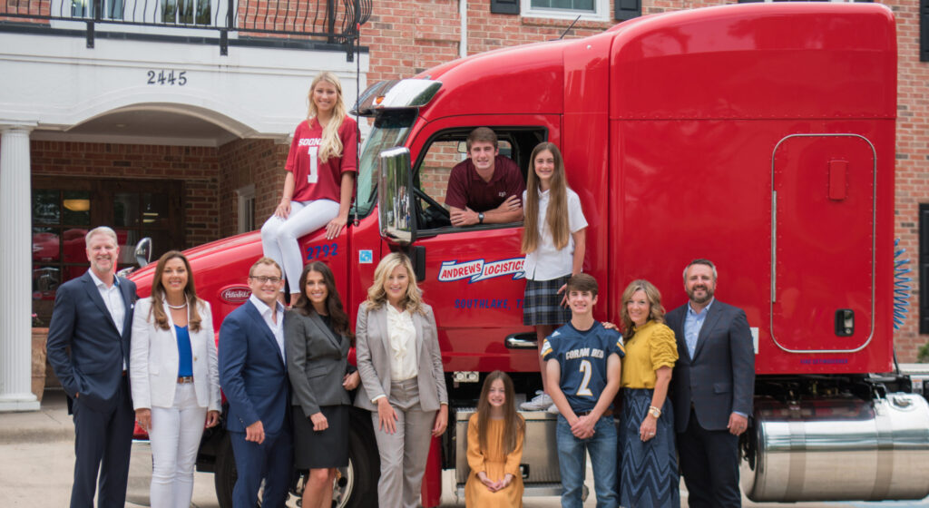Andrews Logistics leadership team and their families in front of a red Peterbilt tractor at the Southlake, Texas headquarters