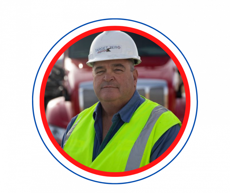 Andrews Logistics driver wearing a Target Zero hard hat and high-visibility vest in front of a red tractor